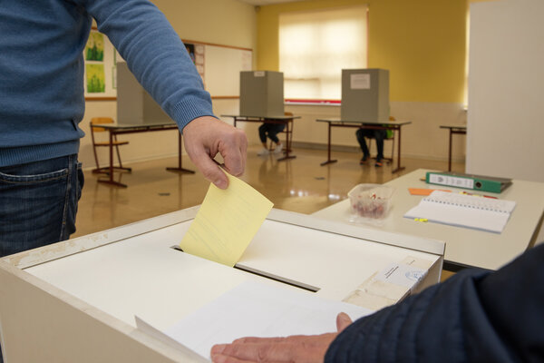 Ein Mann steckt einen Wahlbrief in eine Wahlurne.