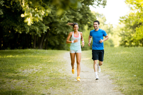 Eine junge Frau und ein junger Mann joggen im Grünen.