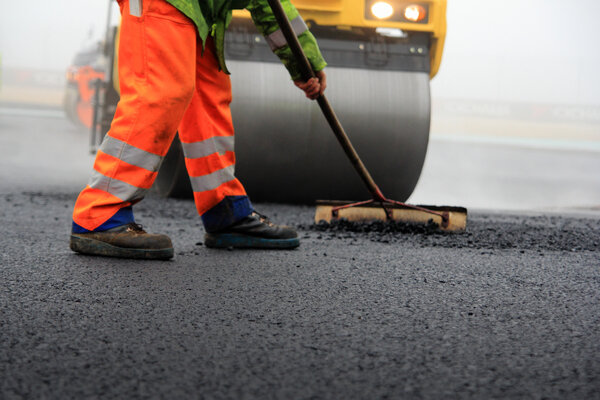 Baustelle: Straßenwalze und Bauarbeiter mit Besen bei der Asphaltfertigung