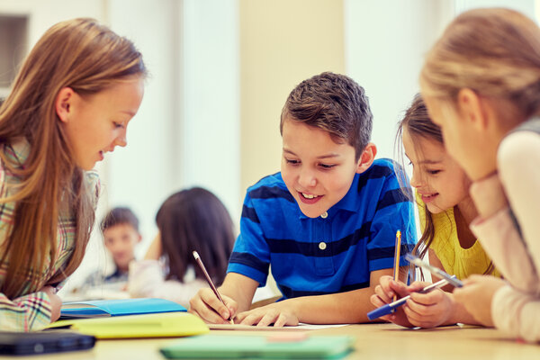 Kinder sitzen in einer Schulklasse zusammen und notieren mit Stiften Erlerntes auf Papier.