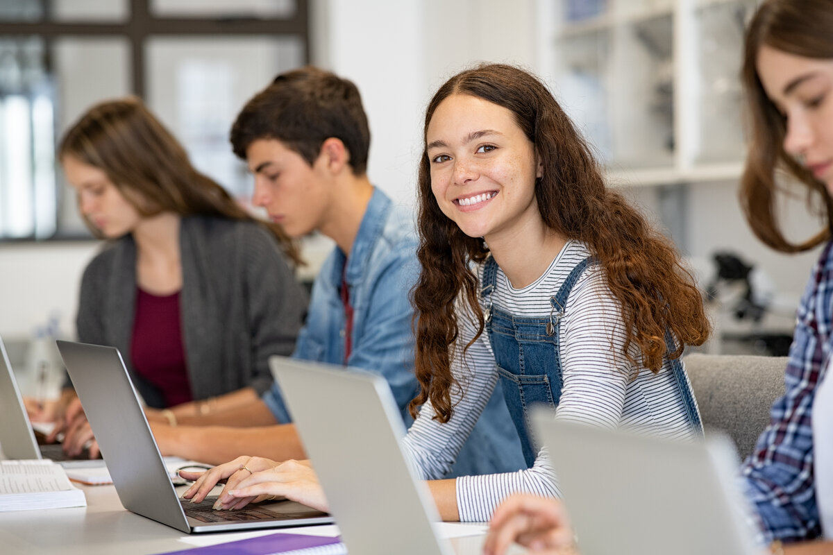 Schülerinnen und Schüler sitzen in einem Klassenzimmer und arbeiten an Laptops.