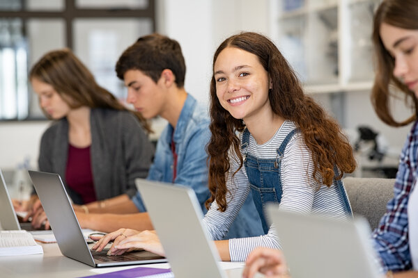 Schülerinnen und Schüler sitzen in einem Klassenzimmer und arbeiten an Laptops.